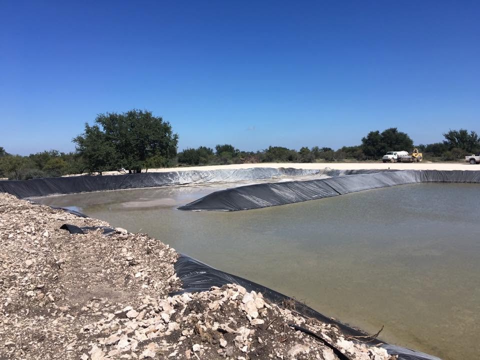 Large stock pond with black liner filling with water, crushed rock banks and brush country in background